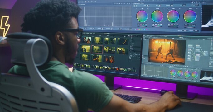 African American colorist edits action movie, makes color correction, works at home. Program interface with RGB tools and wheels on computer and big digital screen. Concept of film post production.
