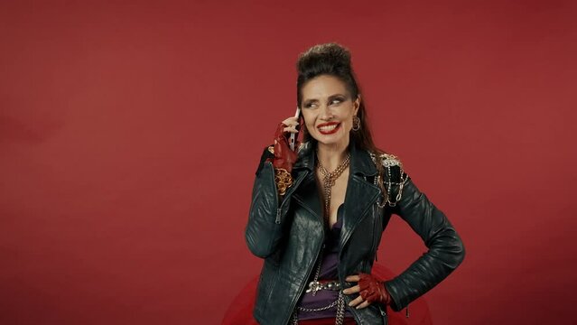 A woman speaks on the phone in a studio on a red background. The woman is embarrassed, flirts, sends a kiss. After finishing the conversation, the woman puts the phone to her chest. Advertising.