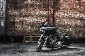 Modern black motorcycle stands against a brick wall background. Advertising poster image.