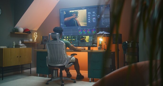 African American colorist edits action movie, makes color correction in professional software on multi-monitor computer and big digital screen, works at home office. Concept of film post production.