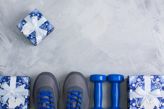 Holiday christmas birthday party sport flat lay composition with gray shoes, blue dumbbells  and blue gifts on gray concrete background. Top view, horizontal orientation