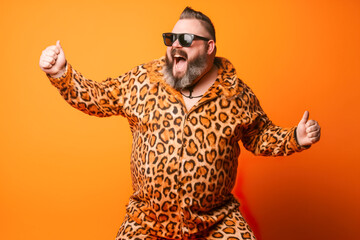 Funny fat man in leopard jumpsuit and sunglasses on orange background