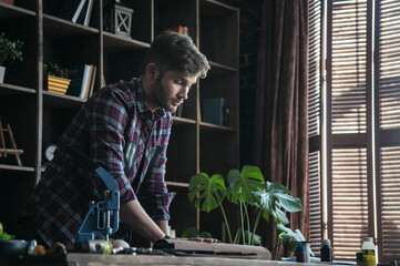 Plan for day. Young man leather maker standing at table and hold roll of brown leather in workshop. Fashion homemade studio. Small business from hobby