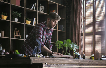 Early morning work. Young man leather worker hold new roll of leather on wooden table in...