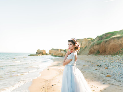 Beautiful brunette bride in light chiffon wedding dress embroidered with beads posing near the sea. Romantic beautiful bride in luxury dress posing on the beach.