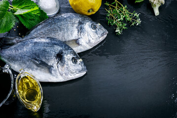 Fresh fish dorado top view. Spicy herb and vegetables healthy food spice on black stone board...