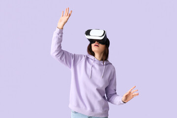 Pretty young woman in VR glasses on lilac background