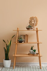 Shelving unit with florariums, books and houseplants near beige wall in room