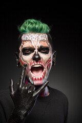 Man with halloween makeup showing tongue. Stylish zombie makeup on mans face, isolated in black background.