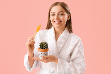 Young woman holding spatula with sugaring paste and cactus on pink background © Pixel-Shot