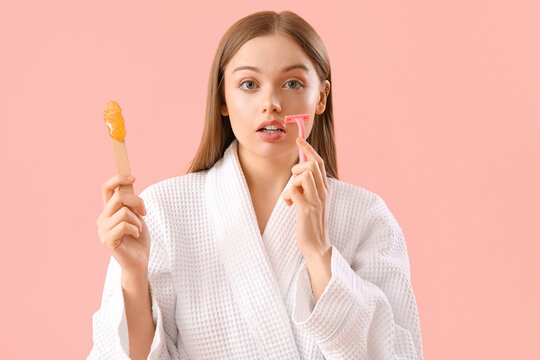 Young woman holding spatula with sugaring paste and razor on pink background