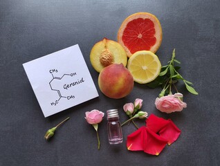 Rose flowers, fresh citrus fruit and cosmetic glass bottle of essential oil with structural chemical formula of geraniol. Geraniol is the main compound found in rose oil. Spa and aromatherapy concept.
