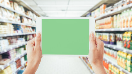 Woman using a digital tablet in the supermarket aisle: shopping, technology and augmented reality...