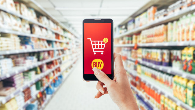 Woman doing grocery shopping at the supermarket, she is purchasing items with a smartphone: augmented reality and commerce concept