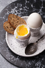 Two soft boiled eggs in eggcups with slice of bread on marble plate. Top view, close up