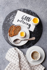 Continental breakfast with soft boiled eggs, slice of bread and freshly brewed coffee over gray concrete background. Top view, flat lay