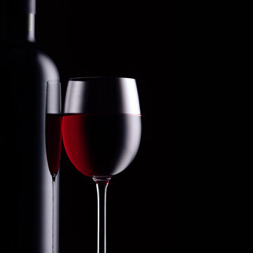 Excellent red wine tasting and celebration: wine bottle and full wineglass on black background