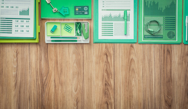 Green office supplies, stationery and financial reports on a wooden desktop, flat lay banner with copy space, green business concept