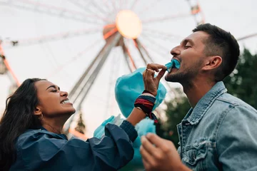 Deurstickers Laughing girlfriend feeding her boyfriend with cotton candy. Young couple having fun in amusement park eat cotton candy. © Artem Varnitsin