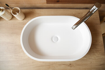 White sink with bath accessories on table near wooden wall