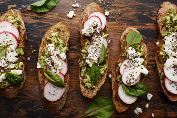 Healthy multi grain bruschetta with radish, chard leaves, tofu cheese, chia seeds and mashed avocado over vintage wooden background. Overhead view, close up - Powered by Adobe