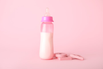 Bottle of milk for baby with toys on pink background