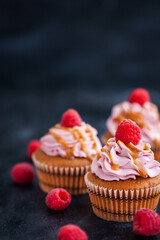 Delicious raspberry and caramel cupcakes on dark background