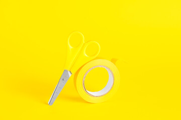 Adhesive tape roll and stationery scissors on yellow background