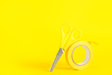Adhesive tape roll and stationery scissors on yellow background