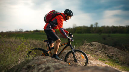 Cyclist in Red Riding the Bike on the Rocky Trail at Evening. Extreme Sport and Enduro Biking Concept.