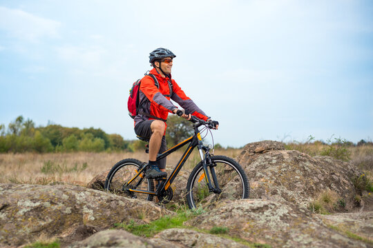 Happy Cyclist in Red Resting on the Bike on the Rocky Trail. Adventure Sport and Travel Biking Concept.