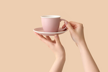 Female hands holding cup and saucer on beige background