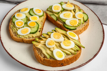 Tasty toasts with quail eggs, avocado and cucumber on white background, closeup