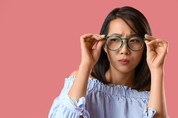 Beautiful Asian woman in stylish eyeglasses squinting on pink background, closeup