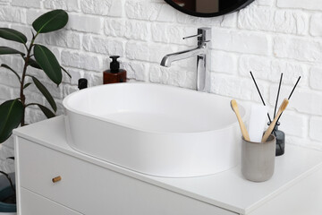 Sink bowl and bath accessories on chest of drawers in bathroom