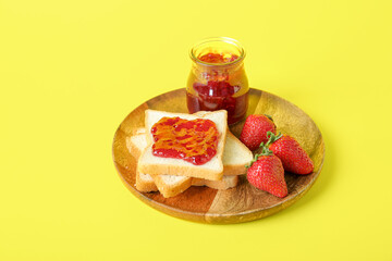 Wooden plate with toasts, jar of tasty jam and fresh strawberry on yellow background