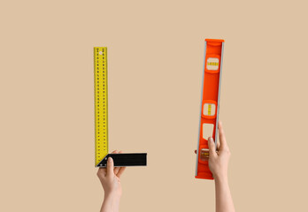 Female hands holding builder's level and square ruler on beige background