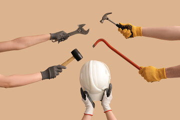 Female and male hands holding different construction tools and safety hardhat on beige background