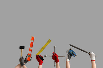 Female and male hands in gloves holding different construction tools on grey background
