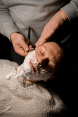 Barber shaving client with vintage straight razor. Classic shave by stainless steel straight edge razor