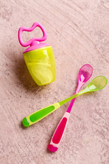 Fototapeta na wymiar Colorful spoons with nibbler for baby on grunge pink background