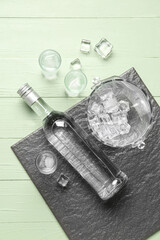 Bottle and glasses of cold vodka on green wooden background