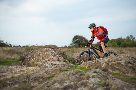 Cyclist in Red Riding the Bike on the Rocky Trail on the Sunset Sky Background. Extreme Sport and Enduro Biking Concept.