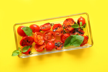 Baking dish with tasty grilled tomatoes and basil on yellow background