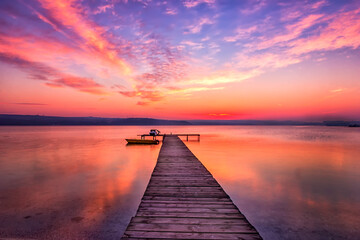 Fototapeta na wymiar Exciting sunset at shore with wooden pier and boat