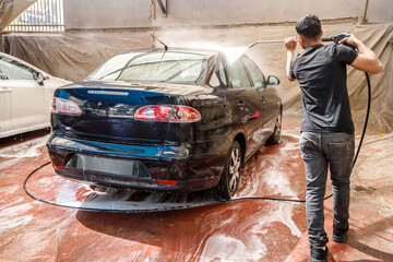 Carwash station outdoor. Worker cleaning automobile, using high pressure water.Carwash station outdoor. Worker cleaning automobile, using high pressure water.
