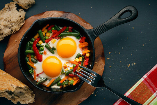 Fried eggs in a cast iron pan with peppers, tomatoes, beans and bread