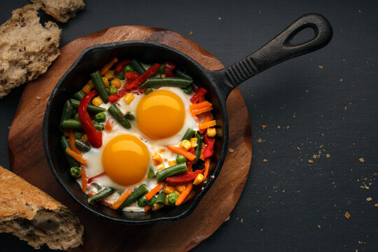 Fried eggs in a cast iron pan with peppers, tomatoes, beans and bread
