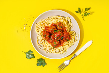 Plate of boiled pasta with tomato sauce and meat balls on yellow background