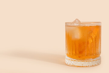 Glass of ice tea with orange on beige background